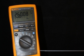 A paper solar cell that has been repeatedly folded is illuminated from below and connected to a voltmeter to demonstrate its output (26 V).