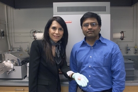 MIT postdoc Gisele Azimi, left, displays three of the 13 different ceramic disks made from oxides of the rare earth elements, with associate professor Kripa Varanasi. Behind them is the furnace used to convert the powdered oxides into solid ceramic form.