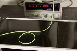 Desktop-scale experiment used to explore the various possible patterns obtained when a thin polymer rod (in green) is deployed onto a moving substrate (black conveyer belt). In this example, the rod forms a periodic array of loops in alternative directions.