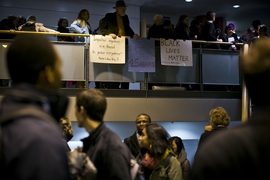 A crowded room with two levels, as second level attendants hold posters in support of Black Lives Matter movement.