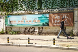 A man walks past a political banner in Guanghua Li that reads, "Patriotism Innovation Inclusiveness Virtue," in Chinese and English.
