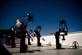 The MEarth-South telescope array, located on Cerro Tololo in Chile, searches for planets by monitoring the brightness of nearby, small stars. This long-exposure photograph shows MEarth-South telescopes observing at night; the blurred telescope is slewing from one star to another.