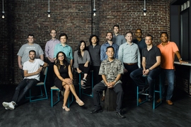 Photo of a dozen or so people in front of a brick wall