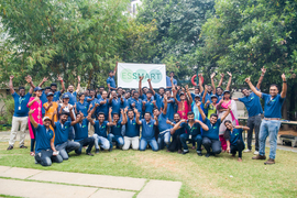 A group photo of the enthusiastic Essmart team, about 40 people, holding the Essmart logo and cheering.