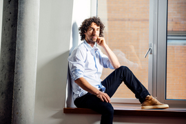 Guy Bresler sits sideways on an indoor window ledge, with elbow resting on raised knee. 