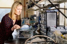 Ellen Roche stands in front of robotic implantable ventilator in a laboratory while wearing a black and red heart polka-dotted dress.