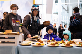 A community member trails two children in line behind a table spread of food on small plates