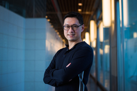 Li, with arms crossed, stands in the middle of a hallway with blue-tinted light in background.