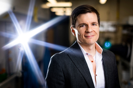 Rob Macfarlane smiles while inside a lab, and a bright spotlight shines in the background.