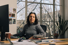 Schlau-Cohen sits inside her office. Family photographs are on the wall, and a large window is in the background.