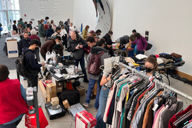 At the mirror lobby of STATA, about 50 people shop at tables and racks of donated items to reuse. Lots of boxes, clothing, electronics and home goods are pictured.