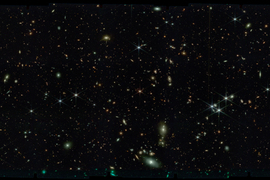 Black space with thousands of stars, tiny swirling galaxies, dozens of very bright glowing lights, and a larger swirling galaxy on bottom right.