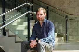 Dean Eckles sits on stairs, with staircase in background. Staircase has metal rails and glass panel sections.