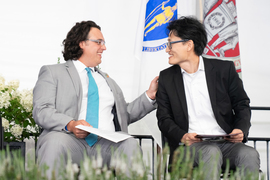 Amos Winter and Jinhua Zhao smile at each other while on stage.