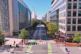 An aerial view down Main street shows the Koch building on the left and Broad institute on right. Bikers, cars, and pedestrians are visible.