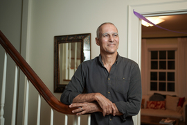 Moungi Bawendi stands with arms resting on a staircase bannister in his home.