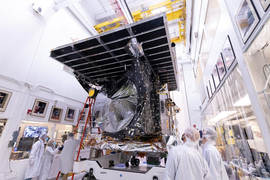 Workers in white protective gear stand near the Psyche spacecraft as it sits on a stand at Astrotech Space Operations facility.