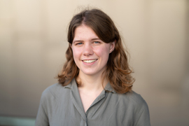 Abigail Schipper smiles for a portrait, with blurry tan background.