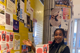 Sophia Ashebir pauses while putting up Agelab posters on a yellow wall.