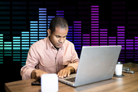 A blind man uses a laptop, and in the background is a bar graph that resembles how audio bars look to show sound.