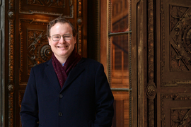 William Deringer smiles and stands next to an ornate wooden door.