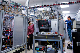 In a lab filled with large machines, computers and wires snaking the ceiling, Li Du stands and checks on something up high. Yu-Kun Lu stands on a step-stool and adjusts something on the other side of the machine.