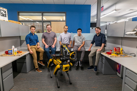 Five guys are in the office around their quadruped robot Spot.