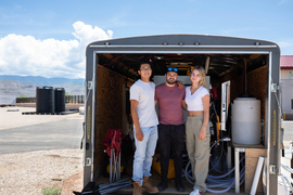 Three people stand inside a trailer with tanks and hoses.