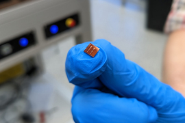 A gloved hand holds a tiny photonic chip.