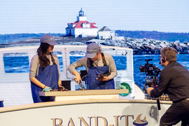 Two people on a fake boat with lobster props demonstrate their hand-held device.