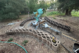 Outside, a robot arm is printing three parts of a curved wall.