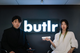 Jiani Zeng, right, and Honghao Deng with a large Butlr logo in between them. They hold the Butlr cylindrical device.